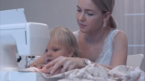 Small child learns new knowledge with her mother using sewing machine Stock Photos