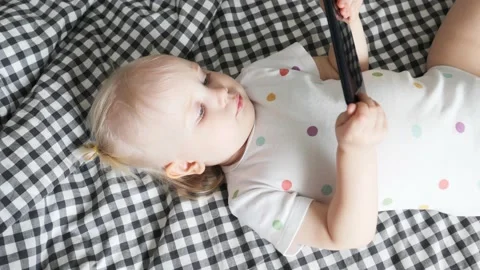 A small child lies on a bed with a cell phone. Baby watching cartoons. Stock Footage 235033568