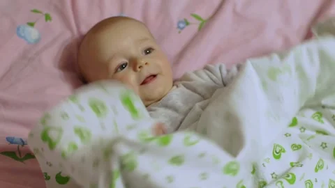 A small child lies on his back, plays with a sheet and smiles. Видео 192330283