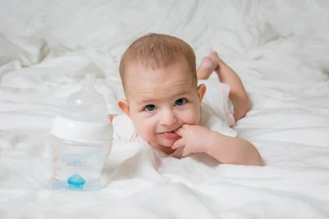 A small child is lying on a white bed on his stomach. The girl put two finger Stock Photos