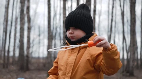 A small child in an orange jacket blows soap bubbles in the forest Stock Footage 305322331