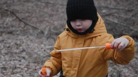 A small child in an orange jacket blows soap bubbles in the forest Stock Footage 305322363