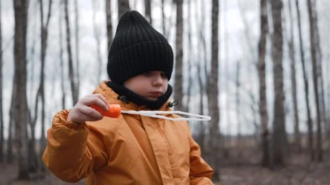 A small child in an orange jacket blows soap bubbles in the forest Stock Footage 305322368