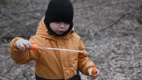 A small child in an orange jacket blows soap bubbles in the forest Stock Footage 305322398
