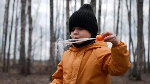 A small child in an orange jacket blows soap bubbles in the forest Stock Photos