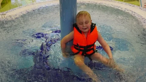 A small child in an orange life jacket sitting in a child pool of Aqua Park. Stock-Footage 122815644