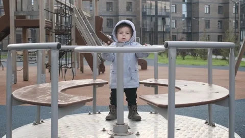 The small child is playing with carousel on a playground outdoors in autumn	 Stock Footage 303948253