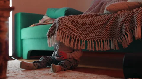 Small child playing hide-and-seek under a woven throw beside a family room .. Stock Footage 343662645