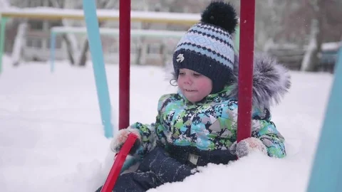 A small child is playing in winter Park. A child on a swing. A Sunny winter day Видео 84851073
