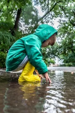 A small child plays sitting in a puddle in rainy weather Stock Photos