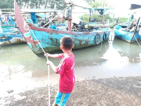 A small child pulling a boat so that it sticks out to the shore Stock Photos