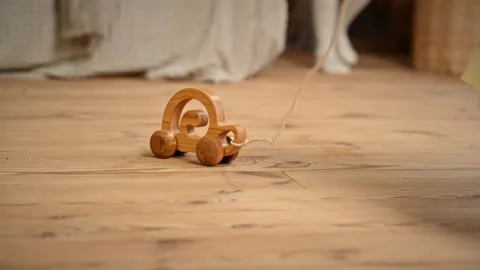 Small child pulling handmade wooden toy car with rope on wooden floor in co.. Stock Footage 339446503