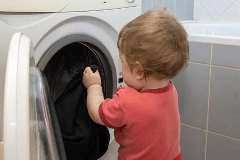 A small child pulls things out of the washing machine, a young assistant 스톡 사진
