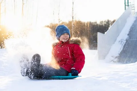 A small child in a red jacket rides down a slide on ice, a cheerful child Stock Photos