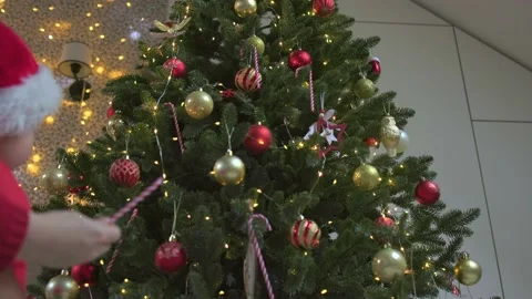 Small child red Santa hat decorates Christmas tree with red white candy cane 動画素材 220917716