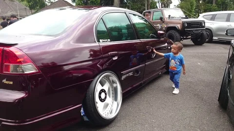 A small child running around a maroon car Stock Footage 290100844