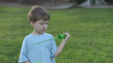 Small child with serious expression blows bubbles in the park. Concentrated boy Stock Footage 317317371