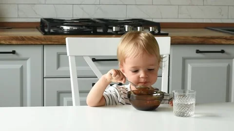 A small child sits and eats himself with a spoon from a plate Video stock 158289799