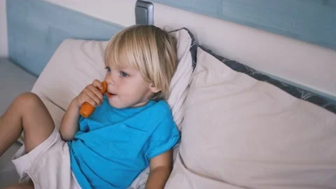 A small child sits on the bed and eats a carrot Stock Footage 220732256