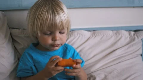 A small child sits on the bed and eats a carrot Video stock 220732364