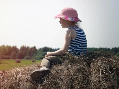 A small child sits on a haystack. Stock Photos