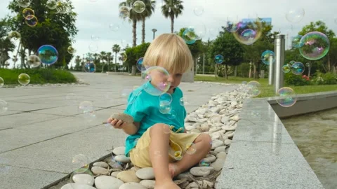 A small child sits on rocks and watches soap bubbles Stock-Footage 200807443