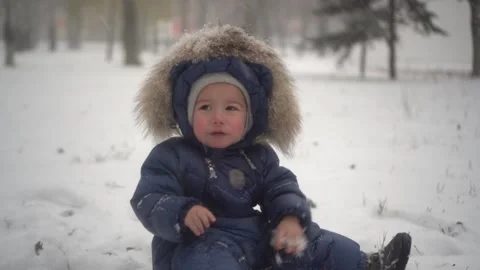 A small child sits in the snow in the park and cries from the cold. The boy in Stock Footage 257565798