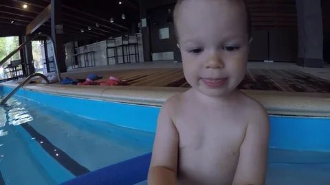A small child sits on the steps in the pool and holds a stick with a camera Stock Footage 111414038