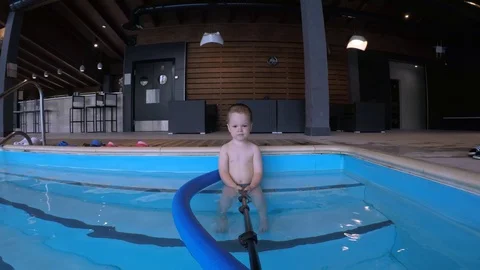 A small child sits on the steps in the pool and holds a stick with a camera Stock Footage 111414171