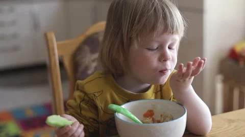 A small child sits at the table and eats organic food from a plate. Stock Footage 239641401