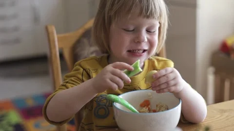 A small child sits at the table and eats organic food from a plate. Stock Footage 239641540