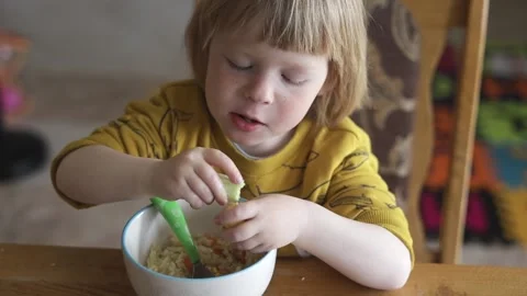 A small child sits at the table and eats organic food from a plate. Stock Footage 239641541