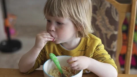 A small child sits at the table and eats organic food from a plate. Stock Footage 239641744