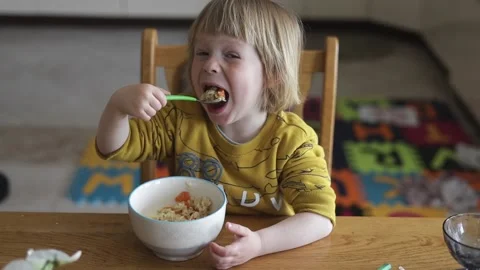 A small child sits at the table and eats organic food from a plate. Stock Footage 239641750