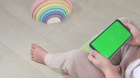 A small child sits on a table with bare legs and uses a mobile phone with a Stock Footage 220614086
