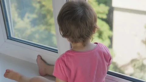 A small child sits on the windowsill and looks out the window at the city. The Video stock 209645561