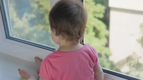 A small child sits on the windowsill and looks out the window at the city. Stock Footage 211132462