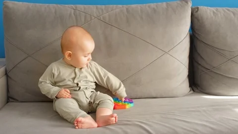 A small child is sitting on the couch with a pop it toy. Laughs and rejoices Stock Footage 155724814