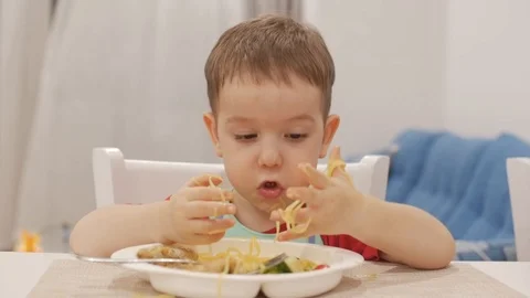 Small Child is Sitting at a Table in a Bib and Eat His Own Spaghetti, the Cute Vidéo 107621767