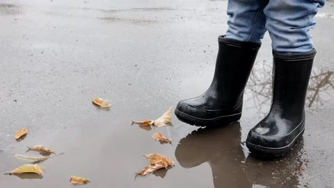 Small child stands in a puddle in rubber boots in autumn Stock Footage 220734908