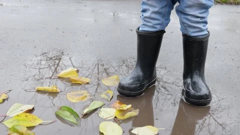 Small child stands in a puddle in rubber boots in autumn Stock Footage 220734909