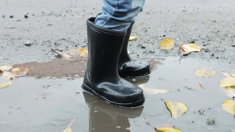 Small child stands in a puddle in rubber boots in autumn Stock Footage 220734966