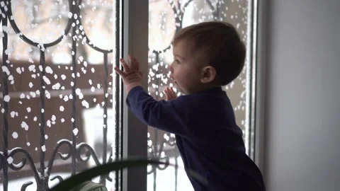 A small child stands on the windowsill and looks out the window. A child knocks Stock Footage 231513654