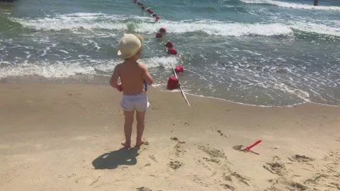 A small child in a straw hat and white shorts plays on the beach by the sea Stock Footage 132301968