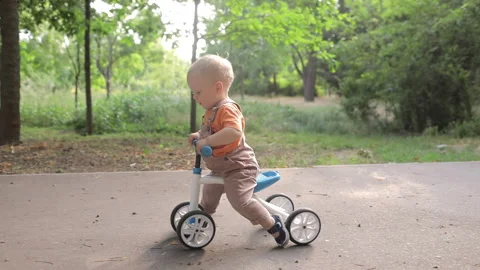 A small child tries to ride a bike in a sunny park Stock Footage 197754553