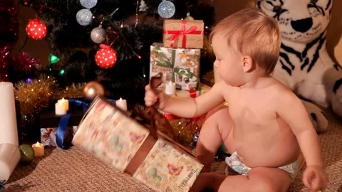 A small child is trying to open a New Year's gift near the Christmas tree Stock Footage 82511207