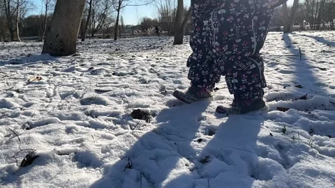 A small child walks through fresh snow. A girl in a down jacket steps on the Stock Footage 295870691