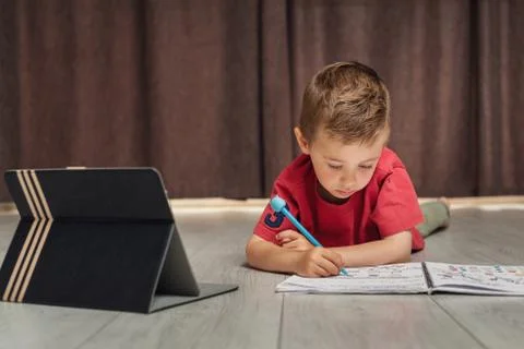 A small child writes in a notebook using a tablet Stock Photos