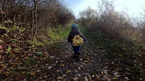 A small child with a yellow bee backpack runs along the path to the mountains. Stock Footage 223722999