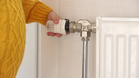 A small child in a yellow sweater opens and closes the valve on the radiator The Stock Footage 219951943